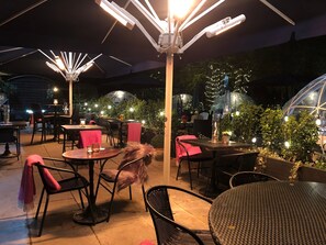 An outdoor dining area with tables and chairs, surrounded by greenery and string lights. - The Churchill Hotel (York)
