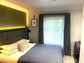 Habitación de hotel con una cama, cabecera estampada con lunares, un cuadro enmarcado en la pared y un ventanal con cortinas.