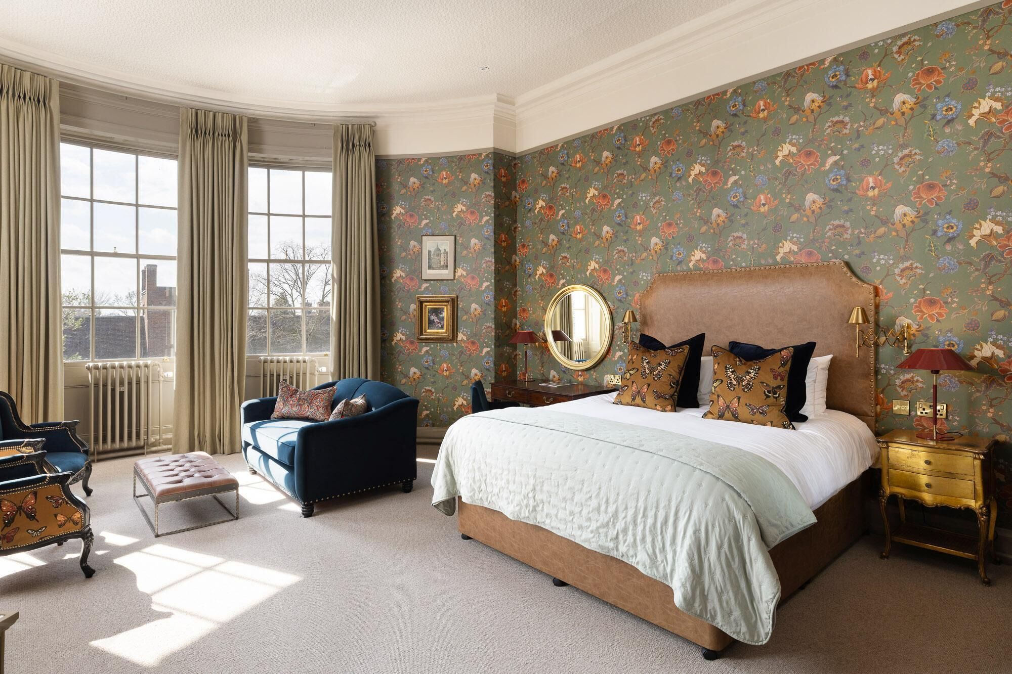 A bedroom with a large bed, a blue armchair, a small table, and a window with curtains.