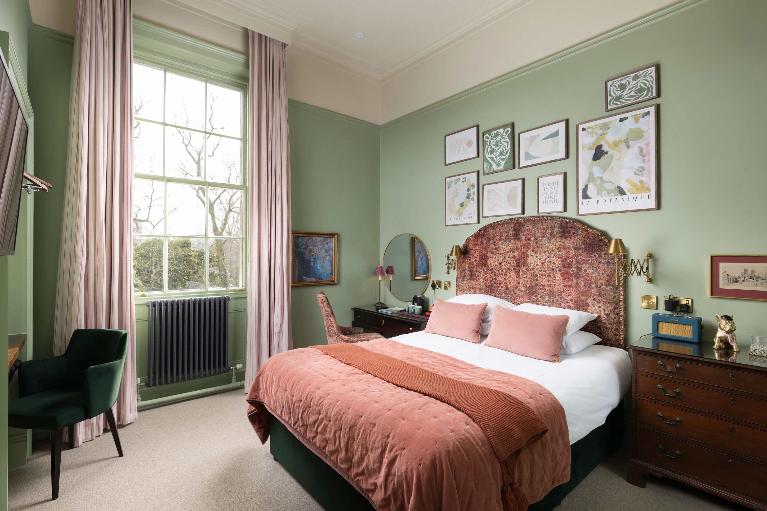 A bedroom with a large bed, a chair, a dresser, a mirror, and artwork on the walls.