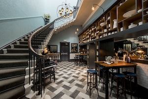 Una imponente escalera con un piano, una zona de bar con taburetes y un candelabro.