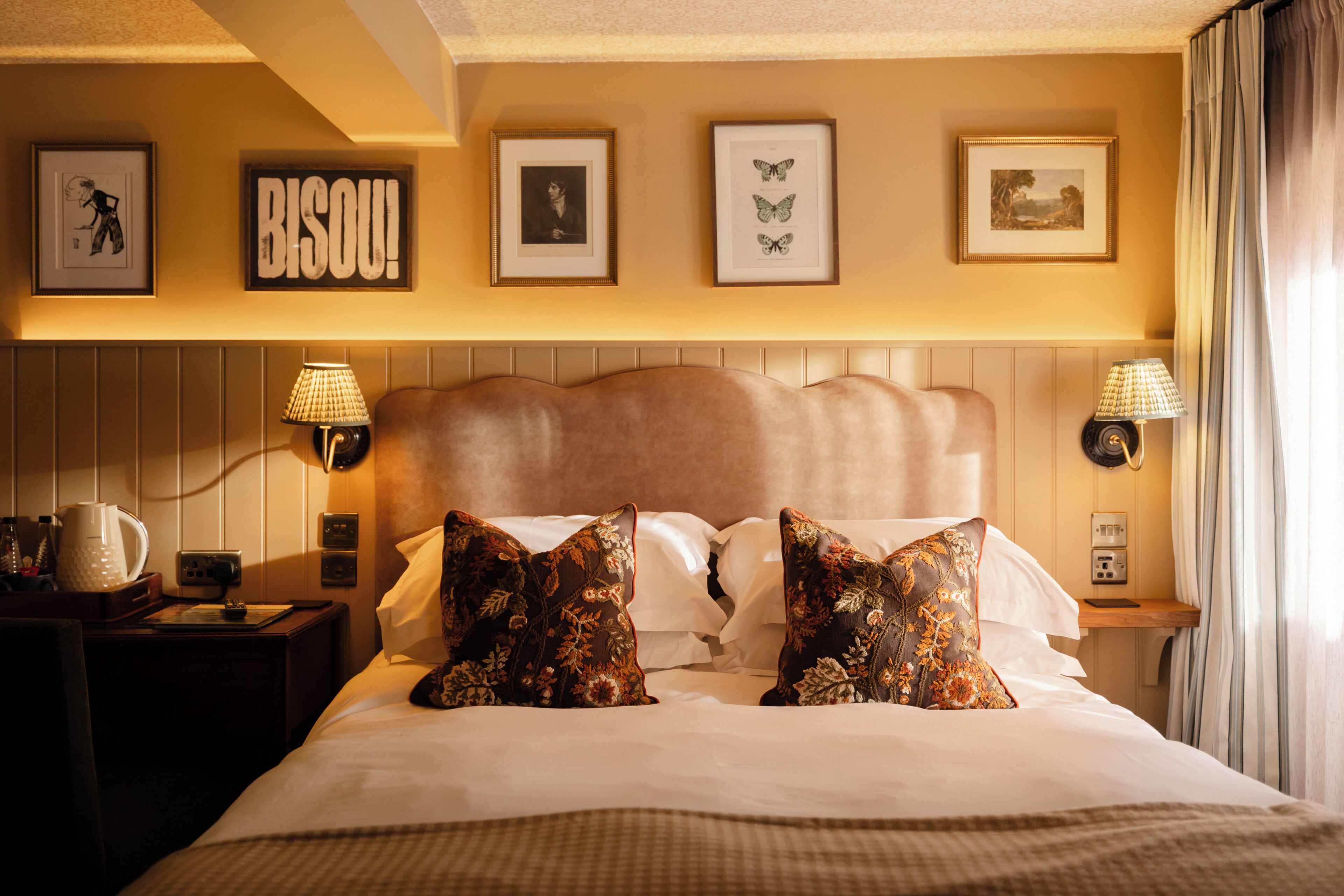 A hotel room with a large bed, two wall-mounted lamps, framed artwork, and a nightstand with a coffee maker.