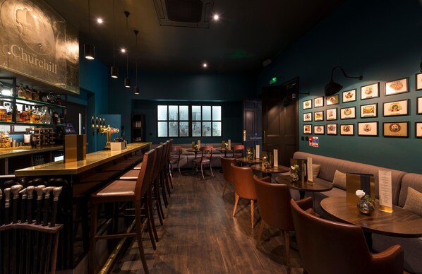 Una zona de bar con mostrador, taburetes y un área de estar con mesas y sillas.