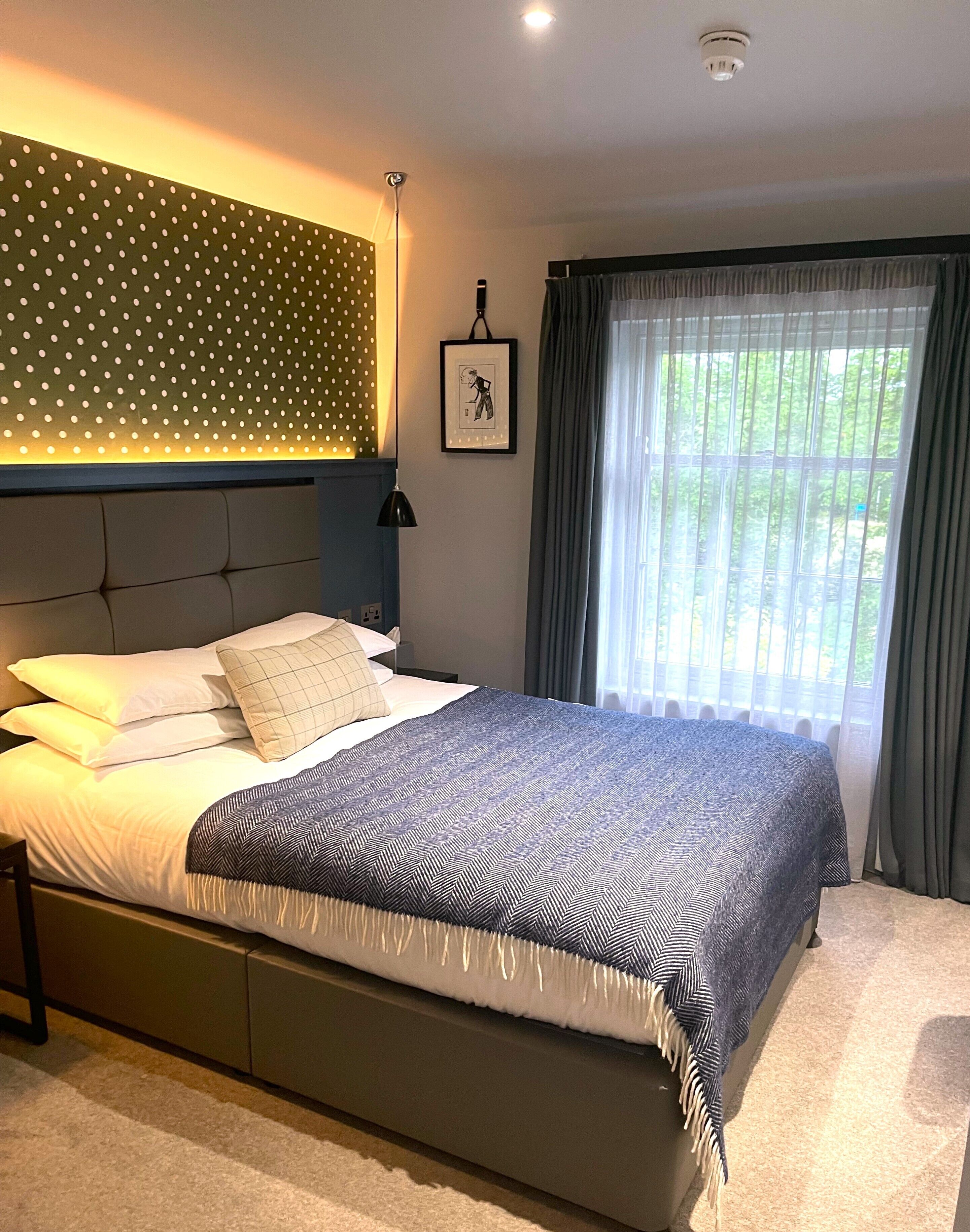 A modern bedroom with a bed, a headboard with a polka dot pattern, a framed picture on the wall, and a window with curtains.