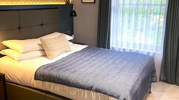 A modern bedroom with a bed, a headboard with a polka dot pattern, a framed picture on the wall, and a window with curtains.