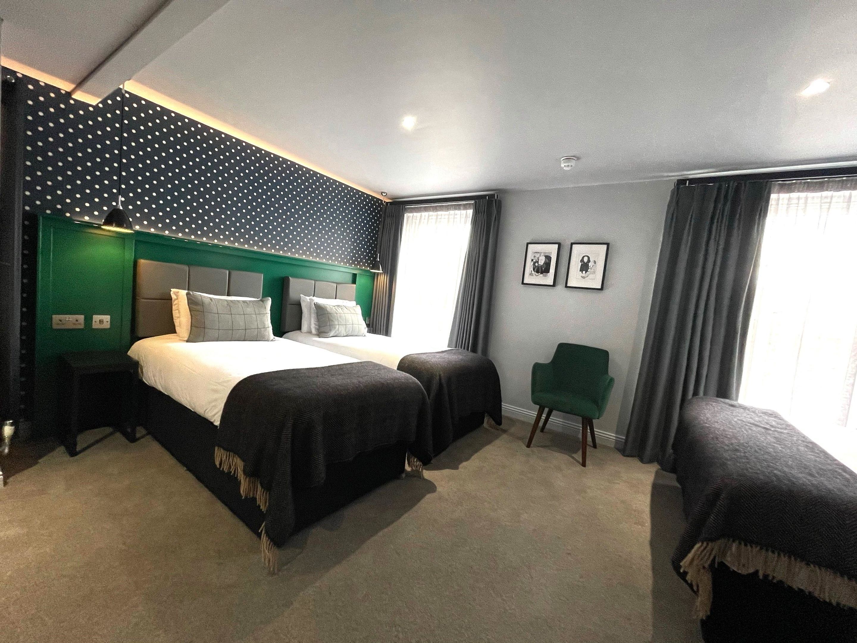 A hotel room with two beds, a green accent wall, a polka dot ceiling, and a green armchair.