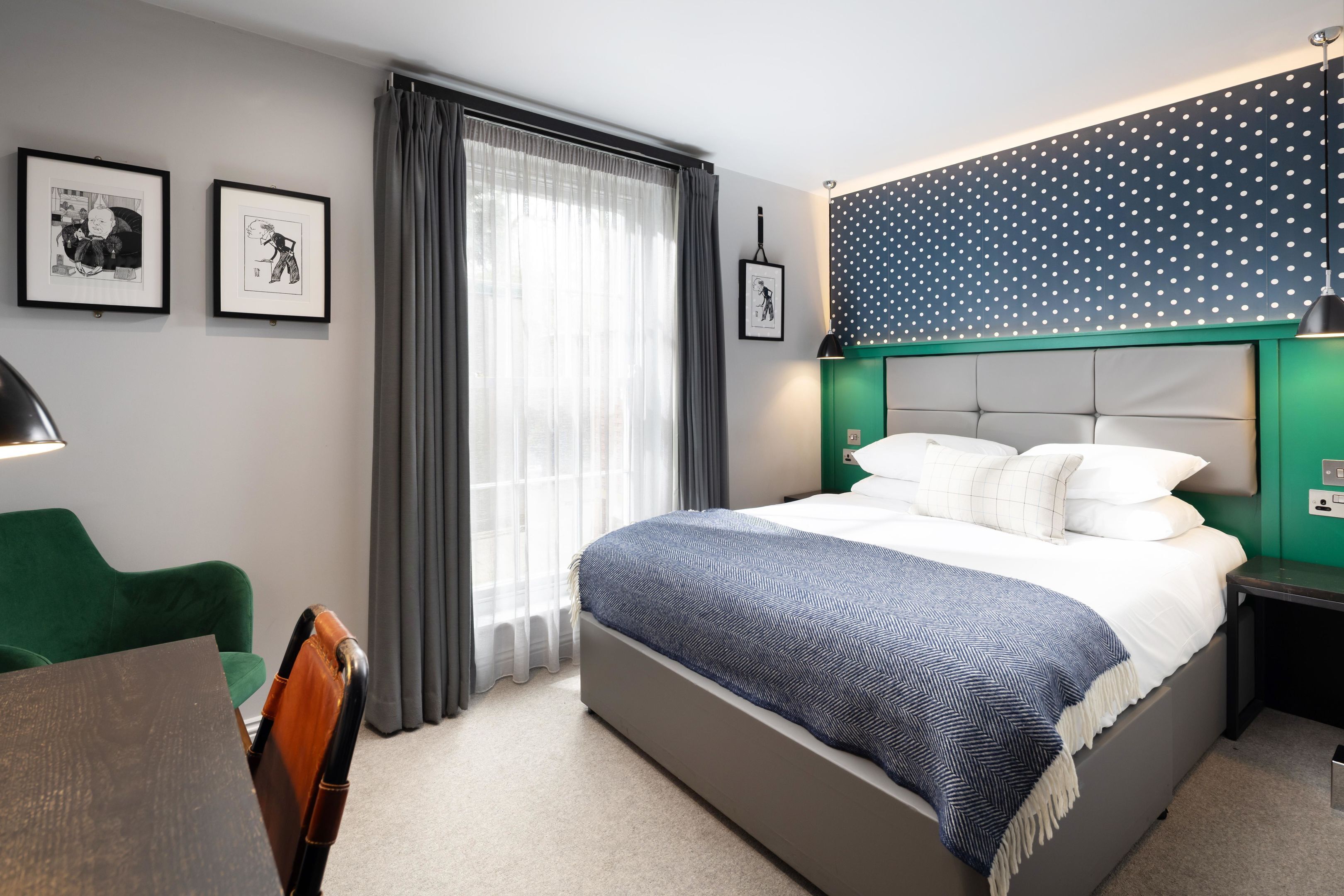 Ein modernes Hotelzimmer mit einem großen Bett, einem Schreibtisch und einem Stuhl. Vor dem Fenster sind Vorhänge, an der Wand hängt ein Bild.