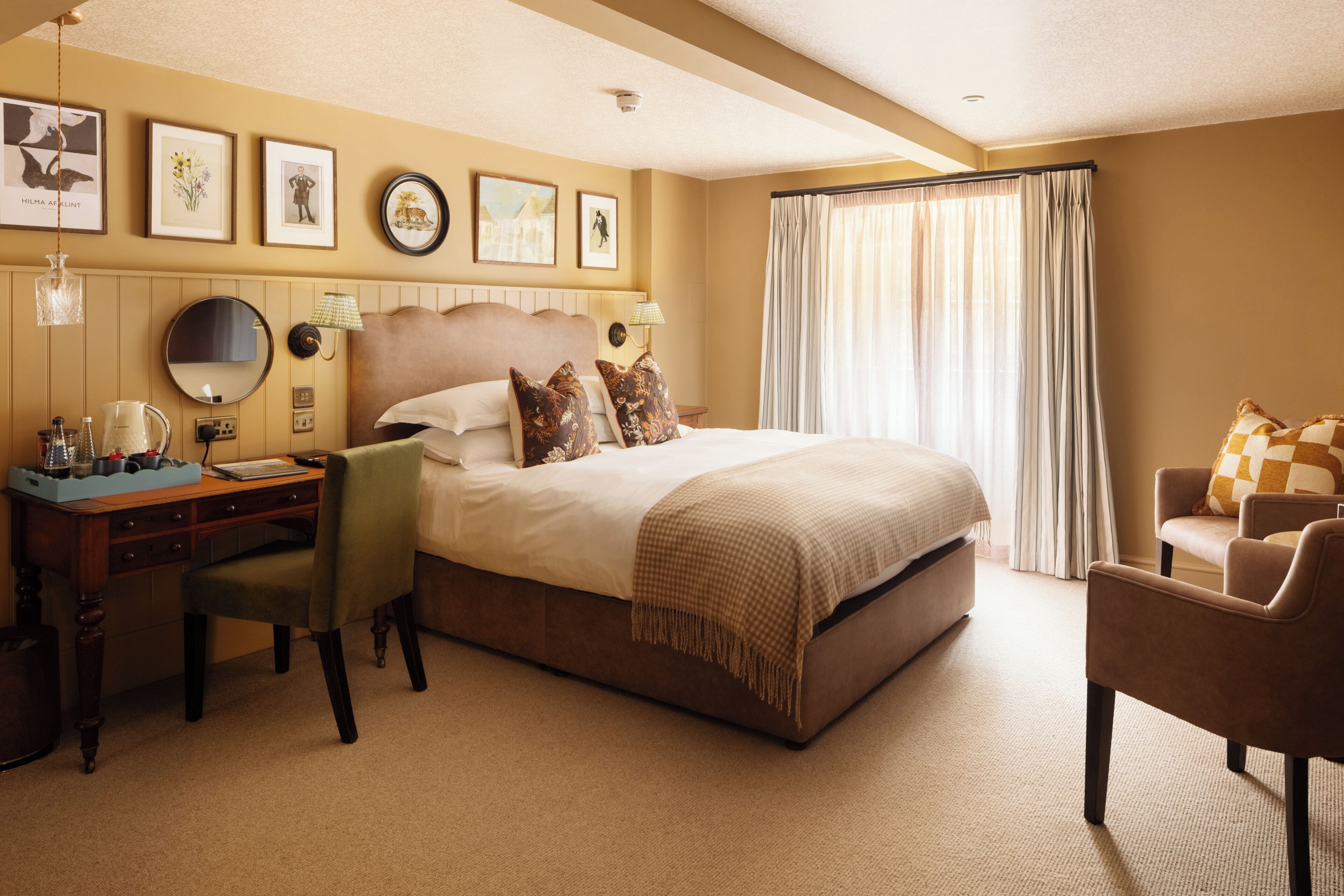 Une chambre d’hôtel avec un lit, un bureau, une chaise et une grande fenêtre avec des rideaux.