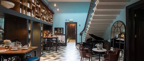 A spacious lobby with a checkered floor, a grand piano, and a staircase leading to an upper level.