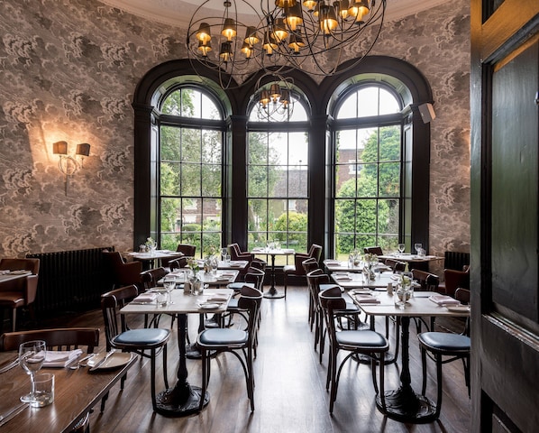Un restaurante con amplias ventanas en arco, mesas y sillas de madera.