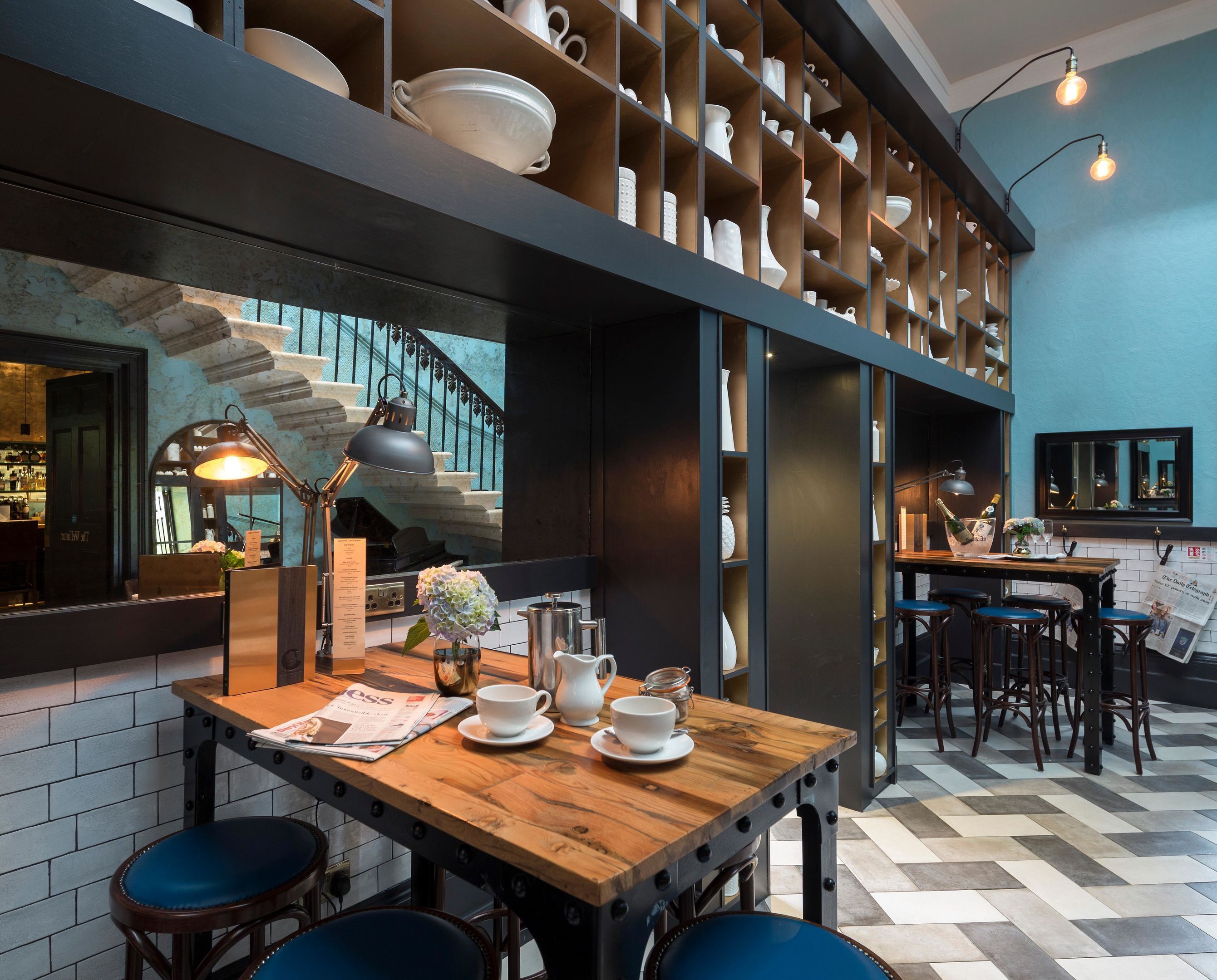 Un interior moderno con una mesa de madera preparada para comer, una zona de bar con taburetes y una cocina visible a través de un ventanal.