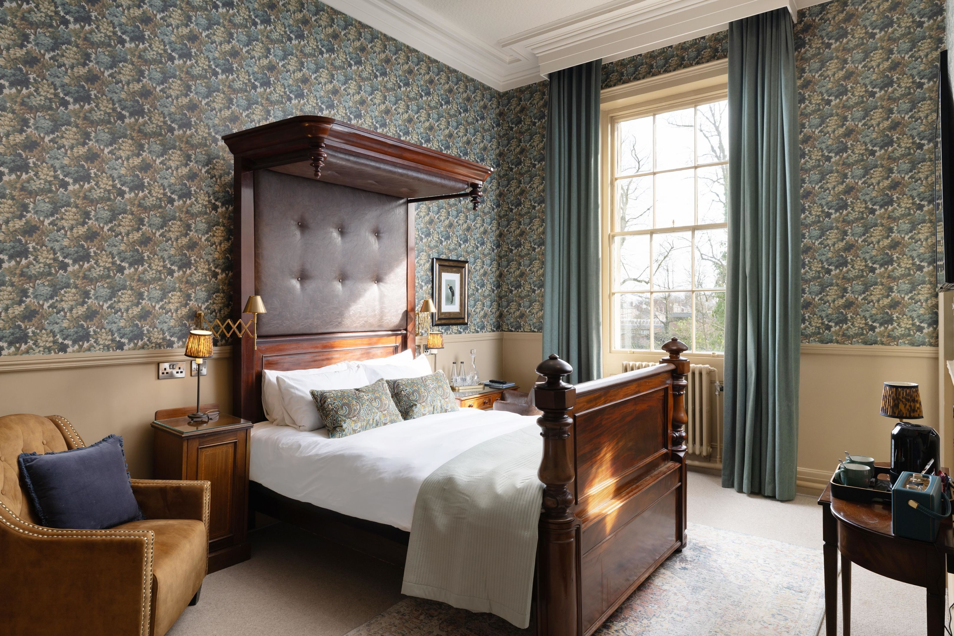 A bedroom with a large bed, a wooden headboard, a nightstand, a chair, and a window with curtains.