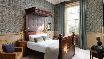 A bedroom with a large bed, a wooden headboard, a nightstand, a chair, and a window with curtains.