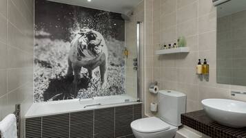 Une salle de bain moderne avec un grand miroir fixé au mur, une baignoire, des toilettes et un lavabo.