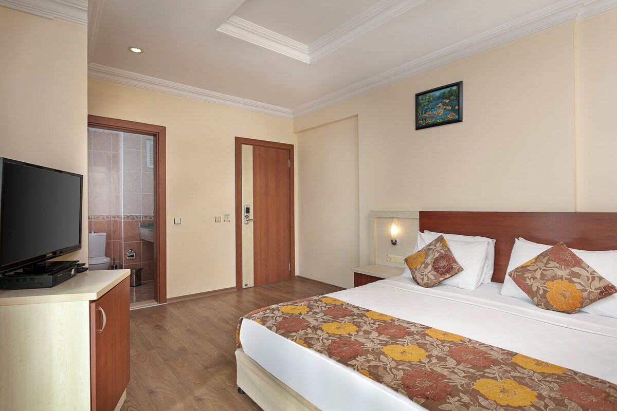 A hotel room with a bed, a television, a nightstand, and a painting on the wall.