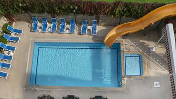 Une piscine extérieure avec un toboggan, des chaises longues et un petit espace détente.