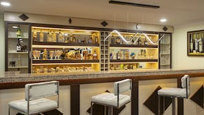 A bar area with multiple shelves of liquor bottles and glasses, two bar stools, and a ceiling light fixture. - Dinc Hotel (Antalya)