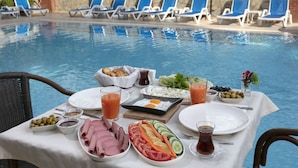 A poolside dining setup with a table set for two, featuring a variety of foods and drinks, surrounded by lounge chairs. - Dinc Hotel (Antalya)