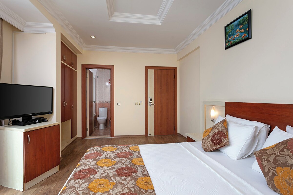 A hotel room with a bed, a television, a wardrobe, and a bathroom visible through an open door.