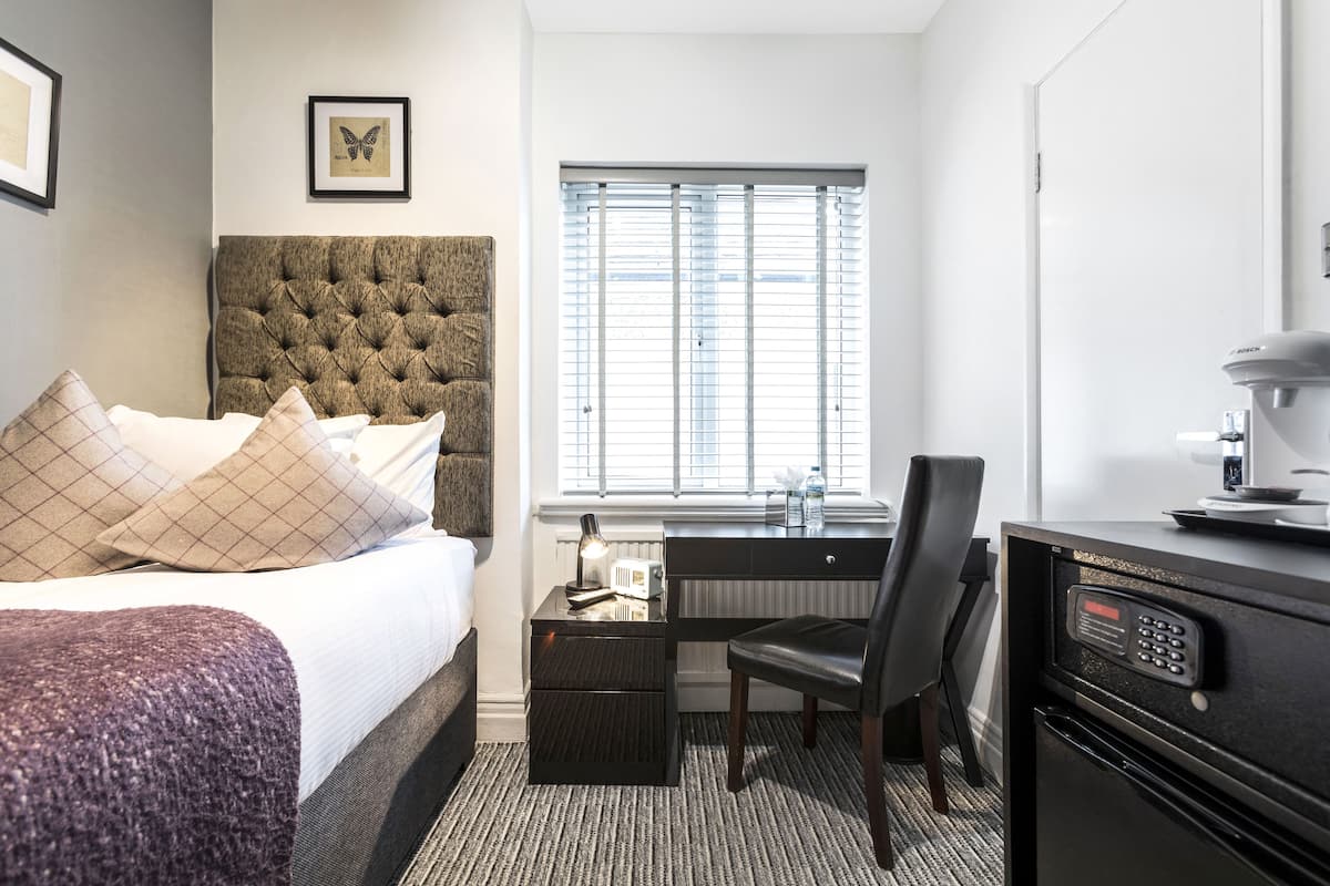 A hotel room with a bed, a desk, a chair, a radiator, and a microwave.
