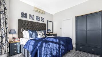 A bedroom with a tufted headboard, a large bed with a blue and white patterned bedspread, a nightstand with a lamp, a dresser, and a wardrobe.