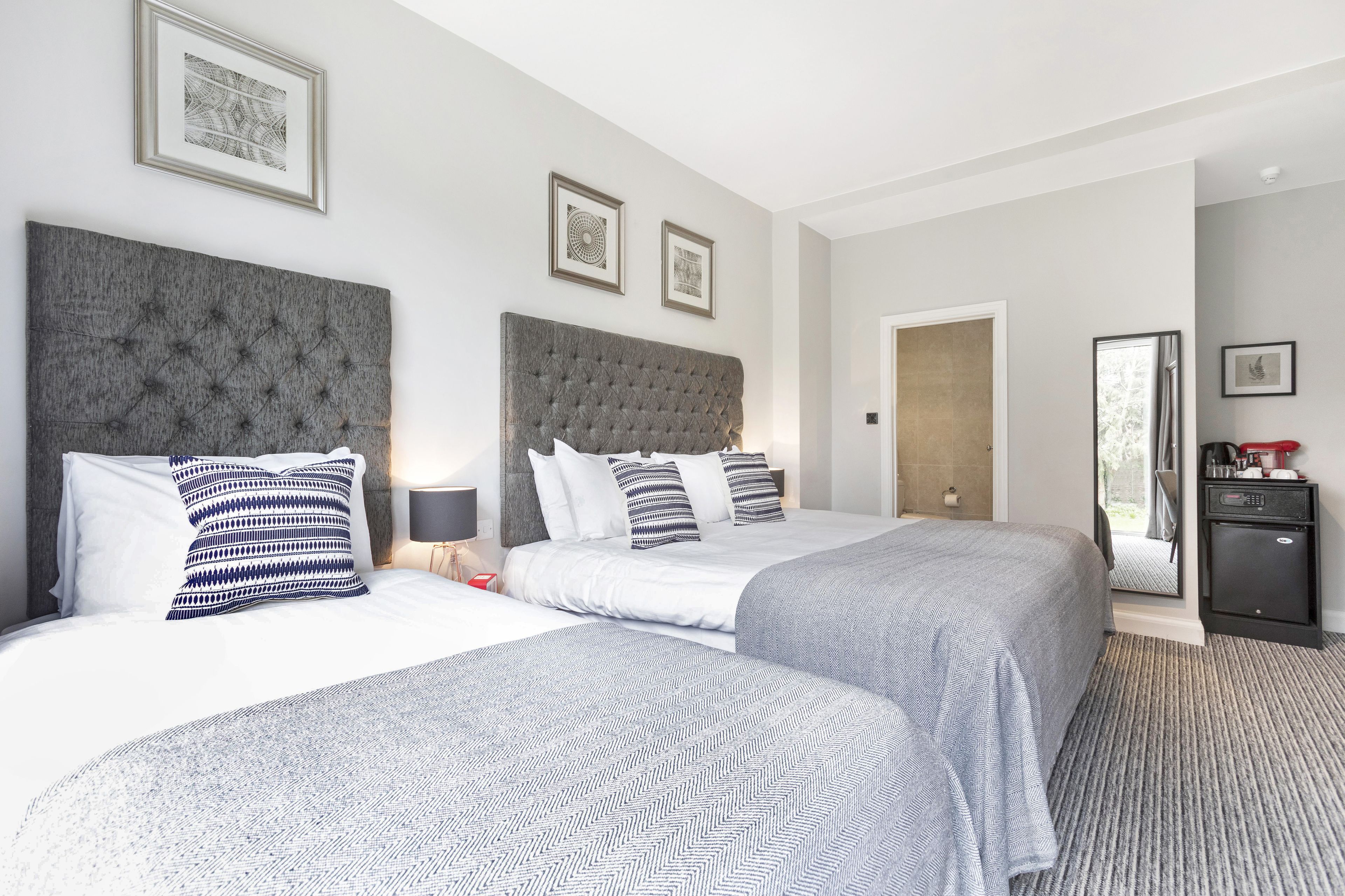 A hotel room with two beds, a grey headboard, a small desk, and a mirror.
