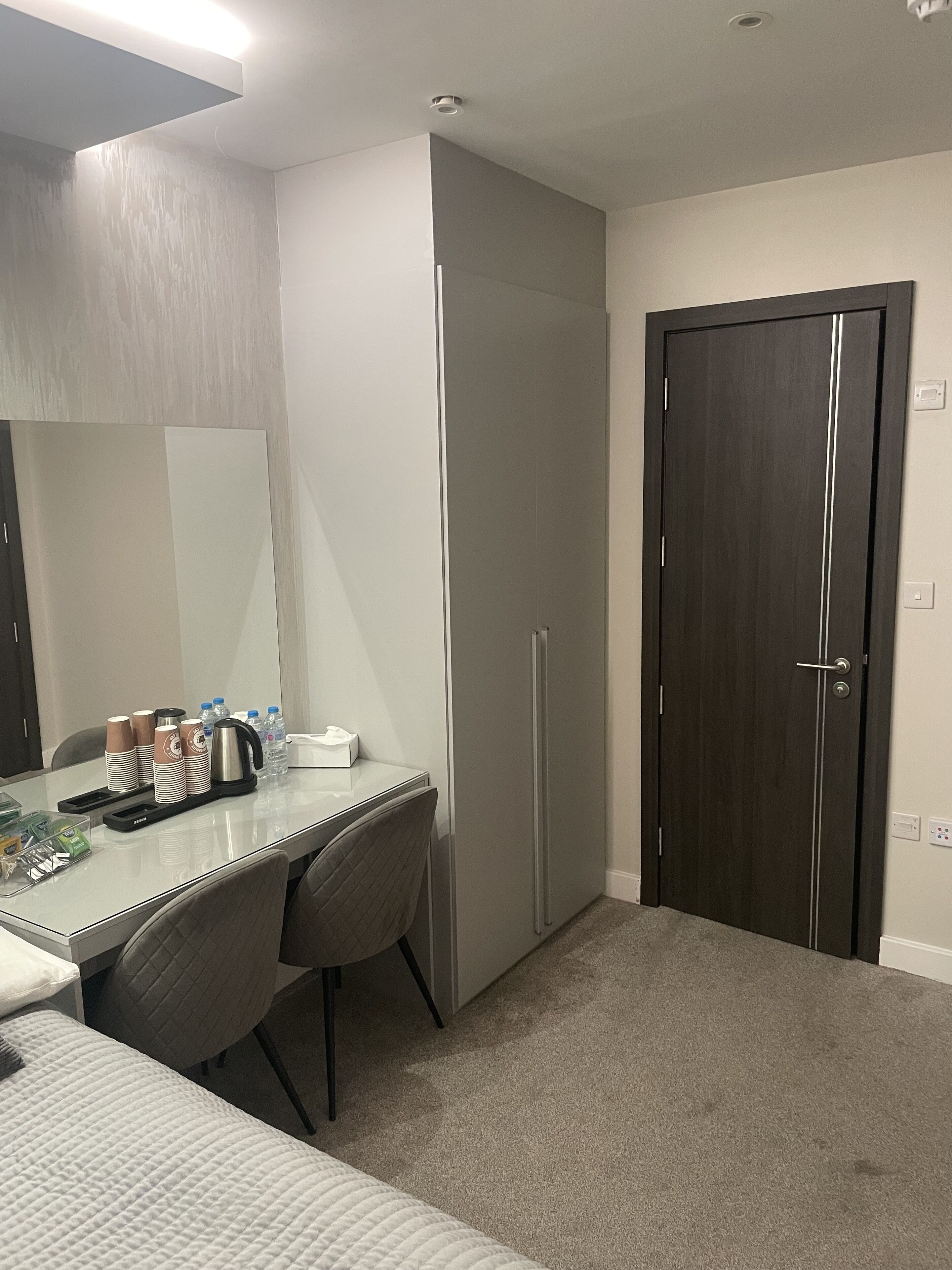 Ett hotellrum med en säng, ett skrivbord med en stol, en garderob och en dörr.