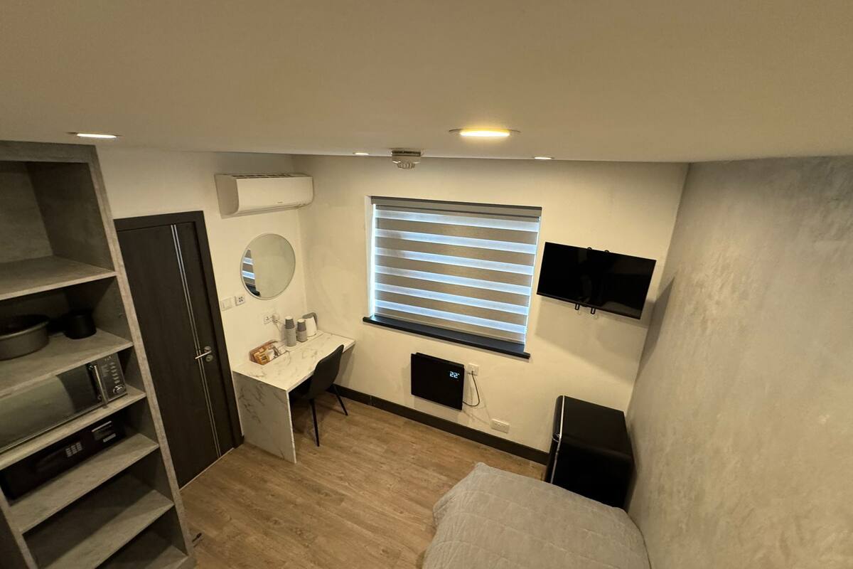 Een kleine kamer met een bed, bureau, spiegel, televisie en een kledingkast.