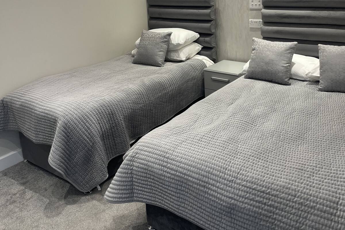 Een moderne slaapkamer met twee bedden, een nachtkastje, een wandlamp en een gestructureerde wand.