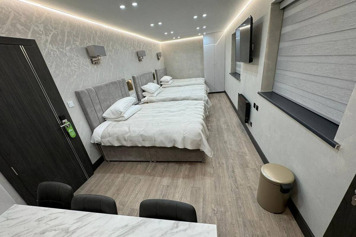 Een moderne hotelkamer met drie bedden, een zithoek en een prullenbak.