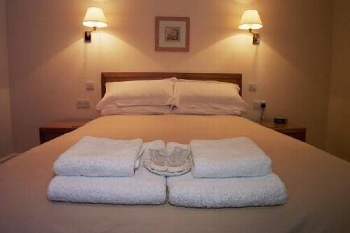 Een net opgemaakt bed met witte lakens en handdoeken in het midden, aan weerszijden twee wandlampen.