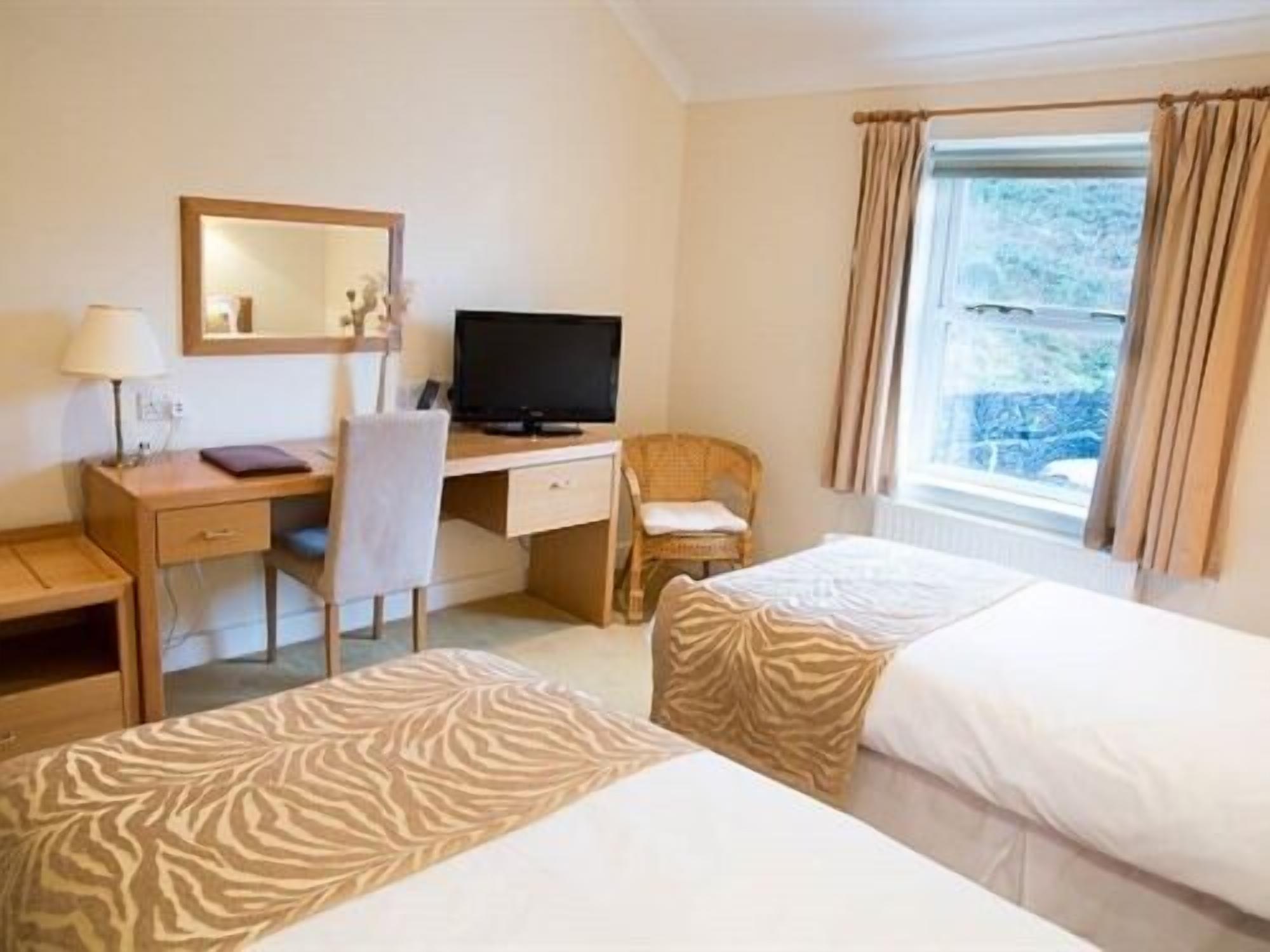 A hotel room with a desk, chair, television, two beds, and a window with curtains.