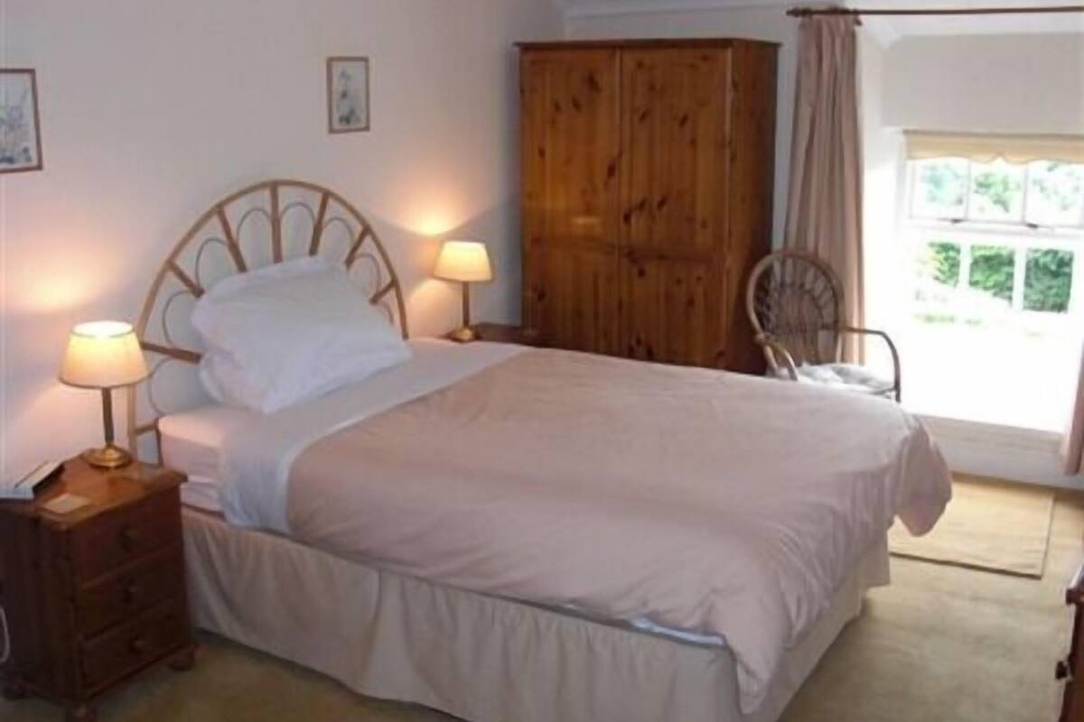 Een slaapkamer met een bed, nachtkastjes, een houten garderobe, een stoel en een raam met gordijnen.