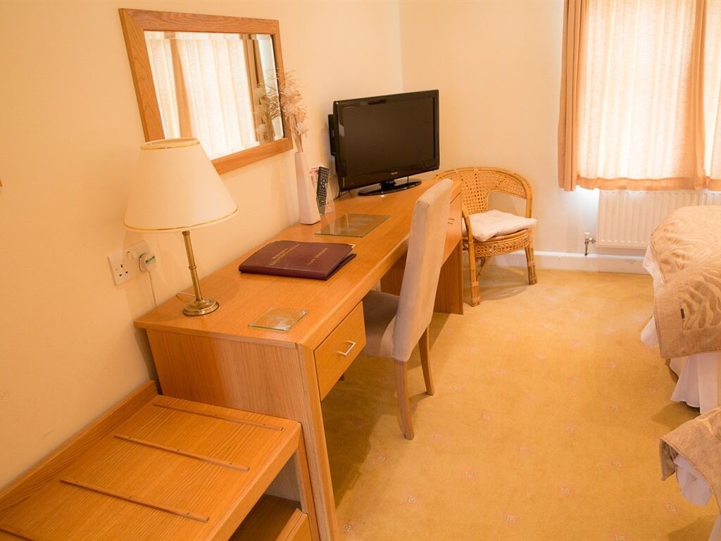 A hotel room with a wooden desk, a television, a chair, a bed, and a lamp.