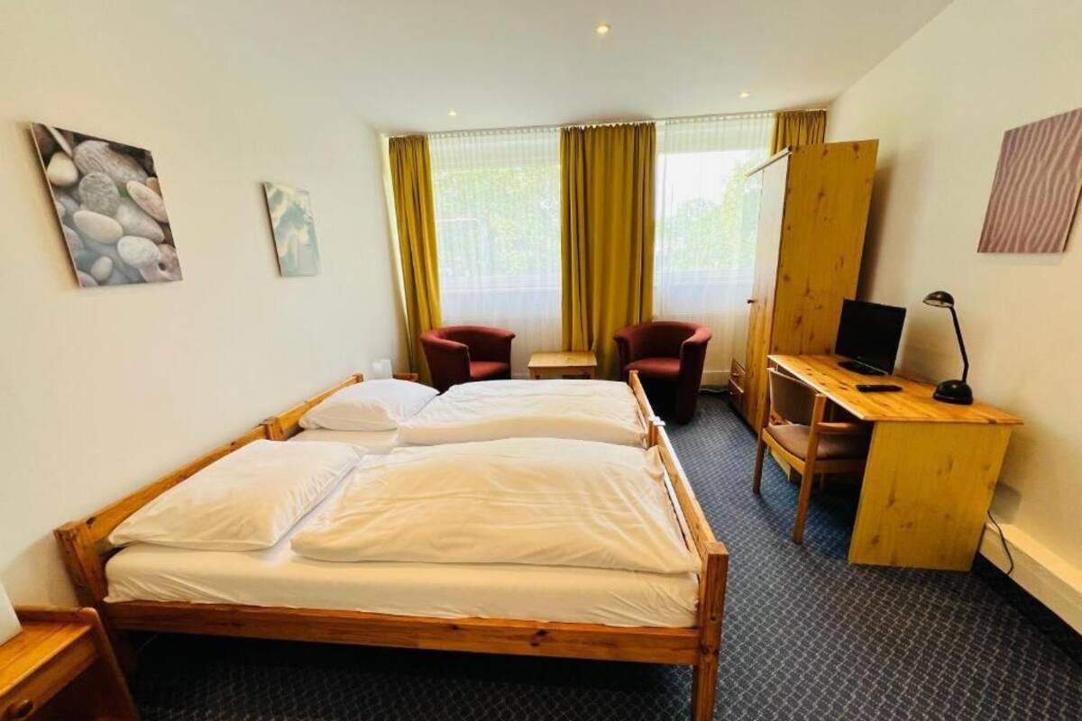 Habitación de hotel con cama doble, dos sillas, un escritorio con una computadora portátil y un ventanal con cortinas.