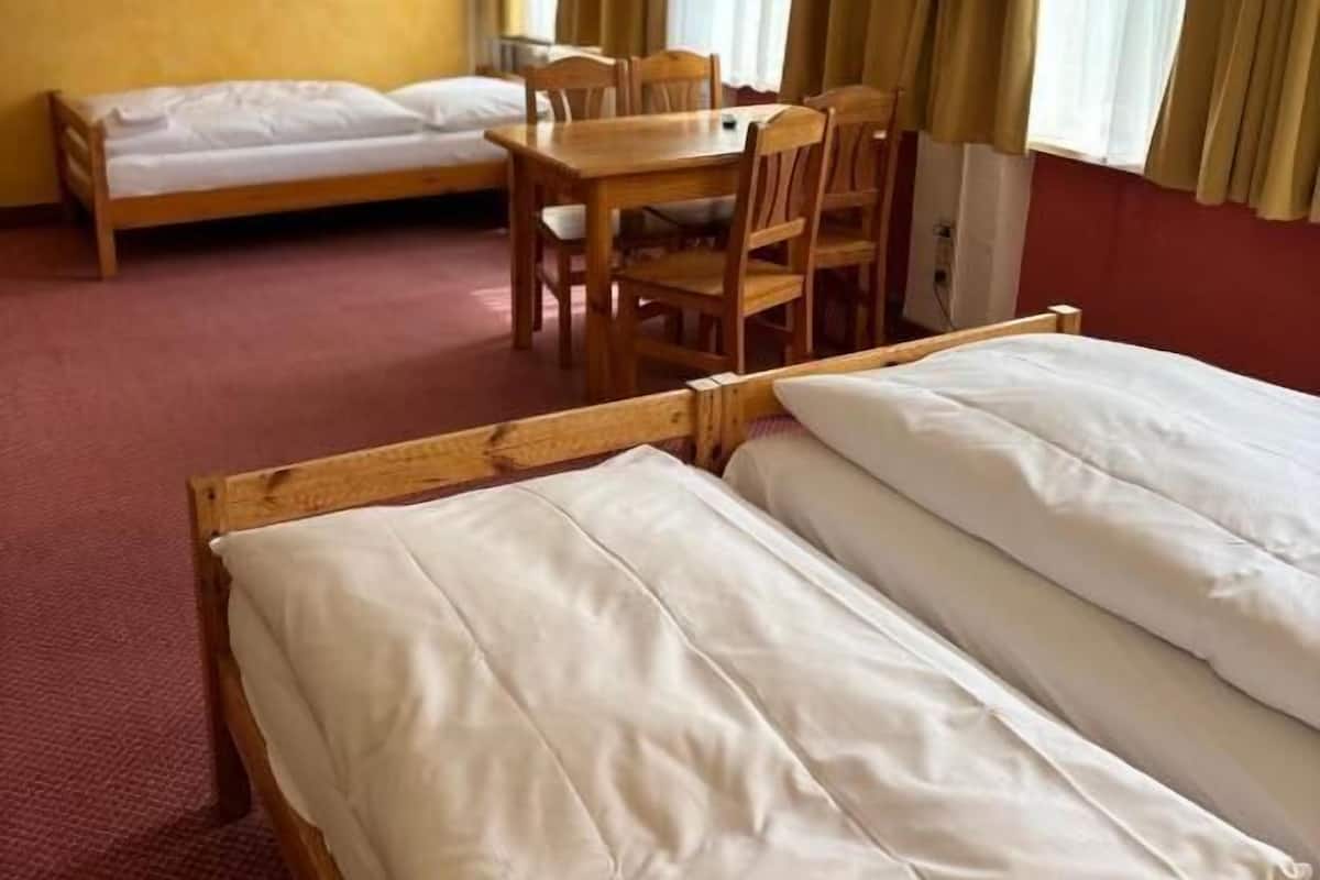 Habitación de hotel con dos camas individuales, una mesa de madera con sillas, un televisor montado en la pared y cortinas en las ventanas.