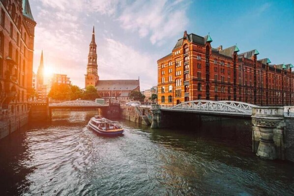 A river with a boat, a bridge, and historic buildings with a tower in the background. - City Apartment Hotel Hamburg (Hamburg)