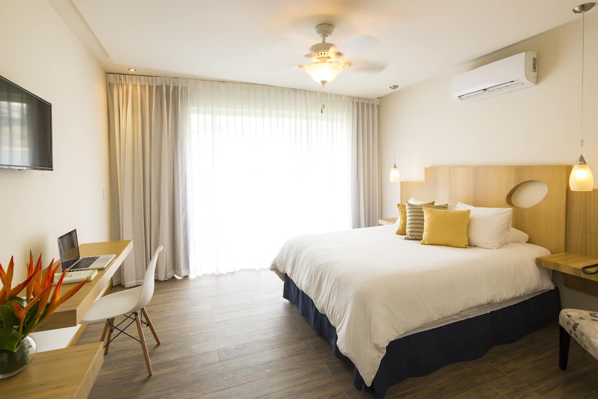 Moderni hotellihuone, jossa on sänky, työpöytä, tuoli ja kattotuuletin.