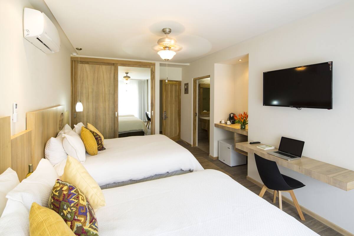 Hotellihuone, jossa on kaksi sänkyä, työpöytä kannettavalla tietokoneella, televisio ja pieni keittokomero.