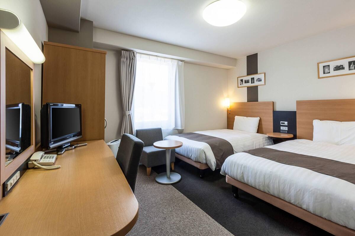 Une chambre d’hôtel équipée d’un bureau, de deux lits, d’une télévision, d’un téléphone et d’une petite table.