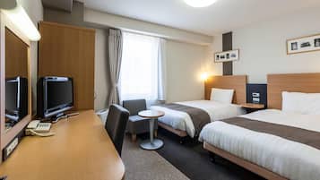 Una habitación de hotel con escritorio, dos camas, televisión, teléfono y una mesita.