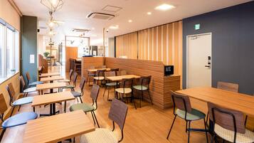A modern cafe with wooden tables and chairs, a counter with a computer, and a view of the city through large windows.