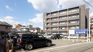 A parking lot with several cars, a building with multiple floors, and a sign indicating a parking area. - Comfort Hotel Shin Yamaguchi (Yamaguchi)