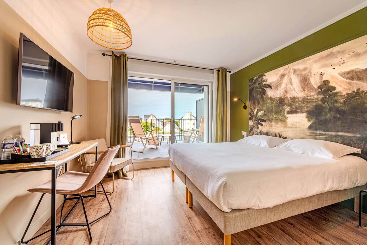 A hotel room with a bed, desk, chair, and a large window with a view of the outside.