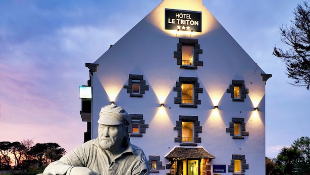 Rakennuksen edessä, kivipenkillä istuvan miehen patsas. Rakennuksen kyltissä lukee: ”Hôtel Le Triton”.