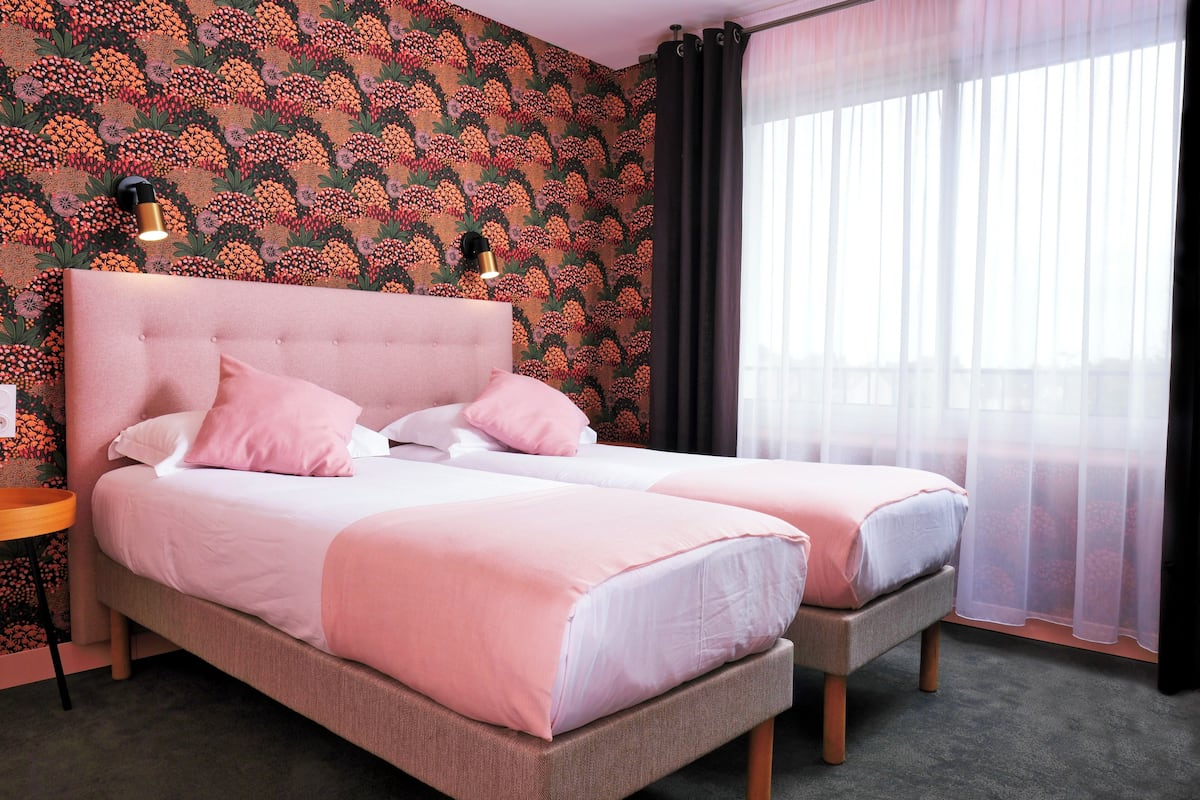 A double bed with a tufted headboard, two bedside tables, and a large window with sheer curtains.