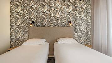 A hotel room with two single beds, a headboard with a floral wallpaper, and two wall-mounted light fixtures.