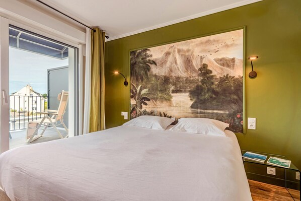 A bedroom with a large bed, a view of a balcony, and a mural on the wall. - The Originals Boutique, Hôtel Spa Le Triton, Roscoff (Roscoff)