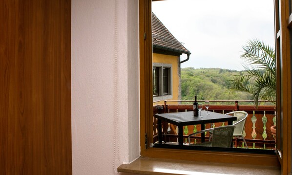 Ein Balkon mit Tisch und Stühlen, der auf ein Haus und üppiges Grün blickt.