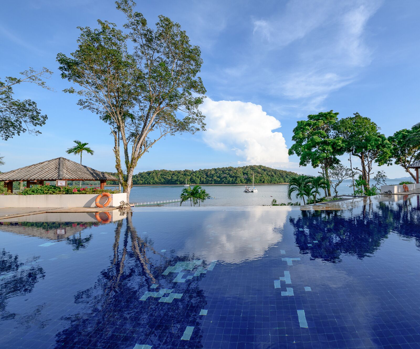 A clear view of a swimming pool with a tiled floor, surrounded by trees and a body of water in the background.